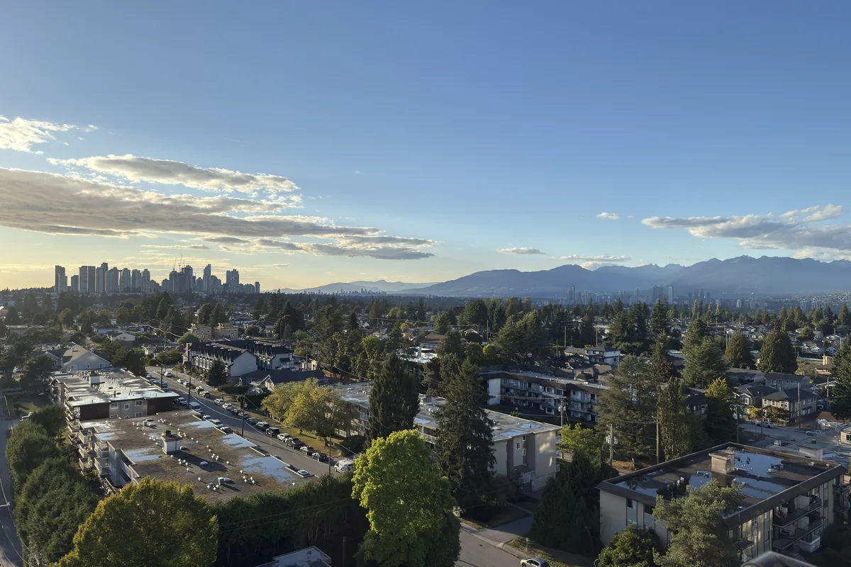 Golden-hour view over a Metro Vancouver neighbourhood with trees, apartments, and mountains on the horizon
